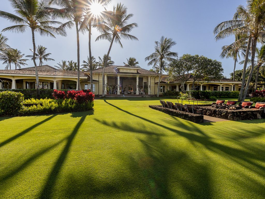 The Great Lawn at Kukui'ula looking back toward the plantation-style Clubhouse, with the lava-rock fire pit seating along the right edge